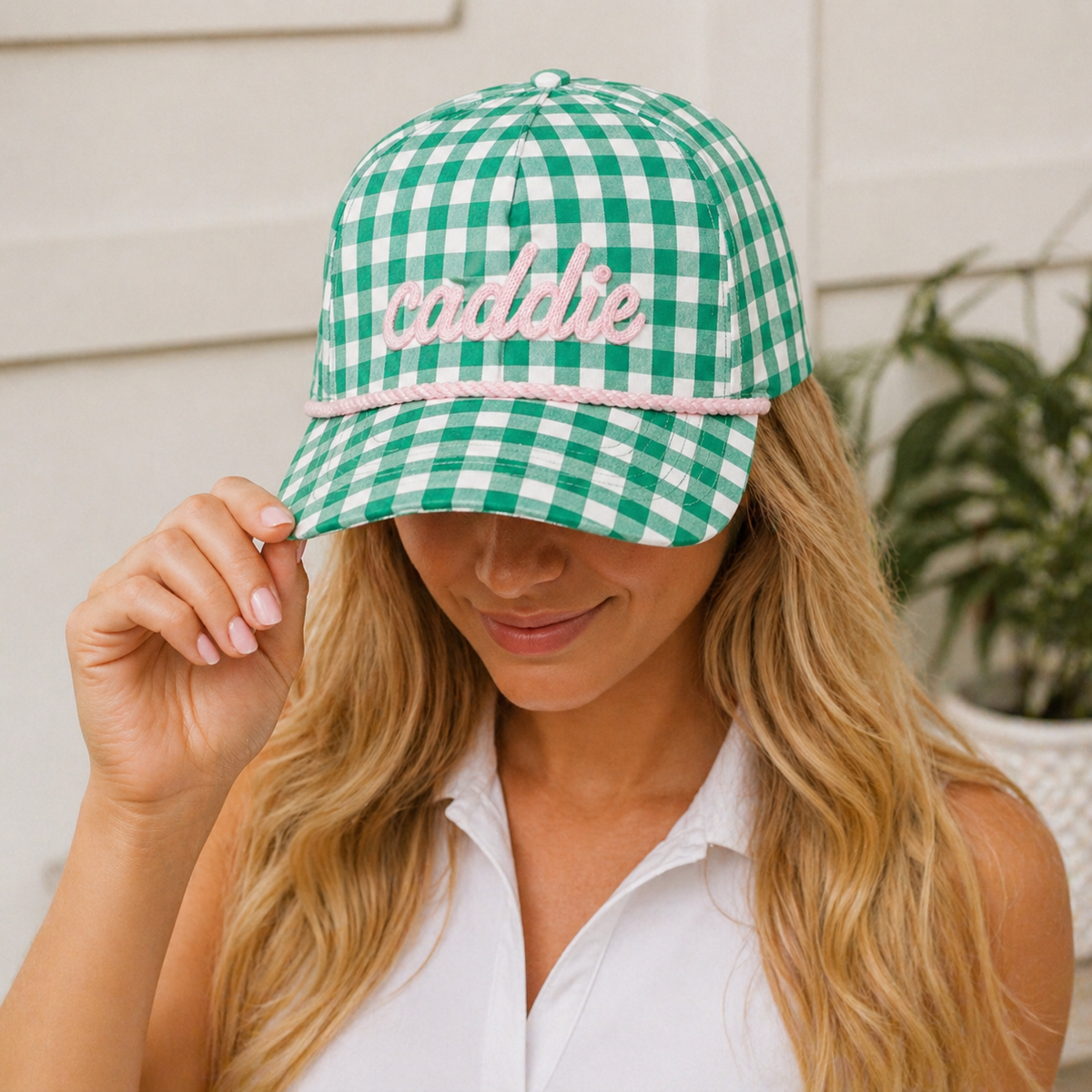 Woman wearing a green and white checkered cap with 'caddie' embroidered on it, outdoors.