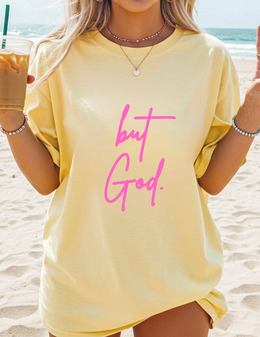 Person wearing a yellow t-shirt with 'but God' in pink text on a beach.