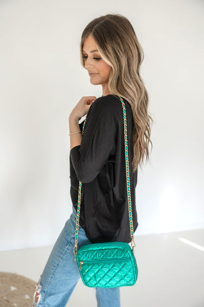 A woman wearing a denim shirt is showcasing a small quilted crossbody bag with a gold chain strap.