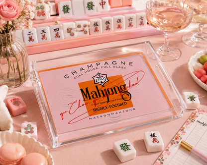 Maison Mahjong packaging on a pink table with mahjong tiles and glasses.