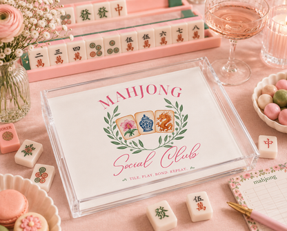 Mahjong set with decorative tiles and 'Mahjong Social Club' packaging on a pink surface.
