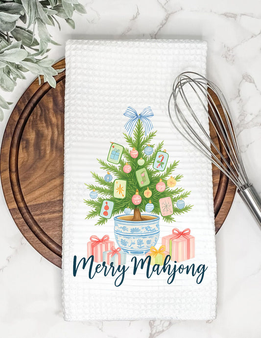 Decorative towel with a Christmas tree and presents design on a marble surface with a whisk and plant.