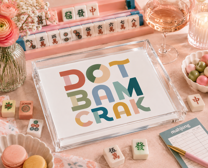 Colorful 'Dot Bam Crak' card on a table with mahjong tiles and wine glasses.