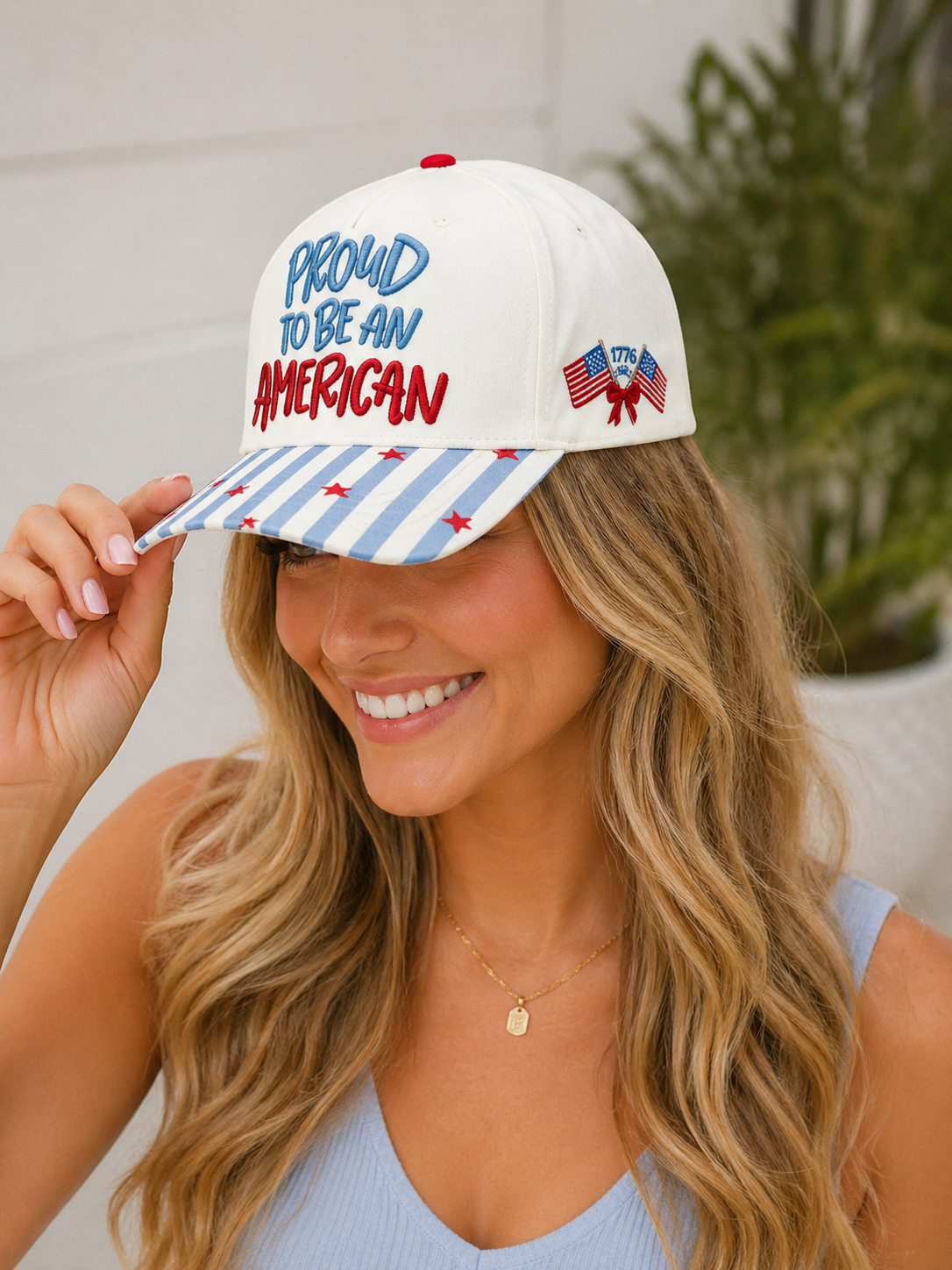 Woman wearing a white cap with 'Proud to be an American' text and an American flag design.