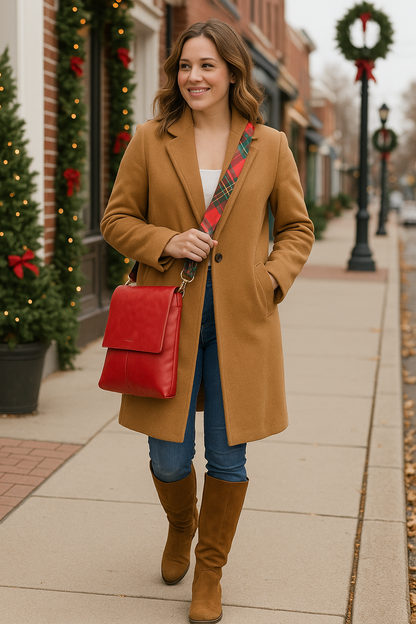 Woman in a tan coat with a red bag walking on a sidewalk decorated for Christmas.